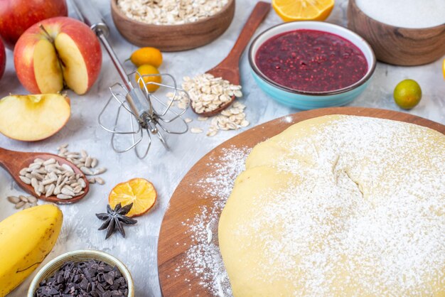 Vista de cerca de la harina de pastelería cruda en el rallador de tablero redondo, frutas frescas, mermelada, galletas, chocolates sobre fondo blanco manchado