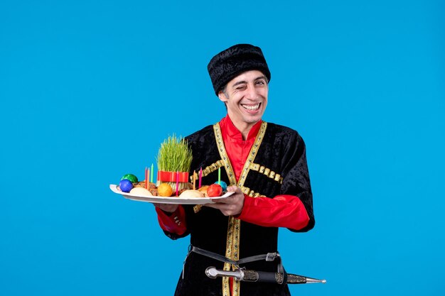 Vista de cerca de un joven con traje tradicional sosteniendo una bandeja llena de dulces nacionales sintiéndose emotivo con el fondo azul