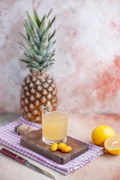 Vista de cerca de jugo de frutas y kumquats en tabla de cortar de madera sobre una toalla despojada de color púrpura, limones y pomelo cortados enteros sobre fondo de colores pastel