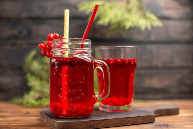 Vista de cerca de jugo de grosella fresca en un vaso y una taza servida con tubo sobre una tabla de cortar de madera