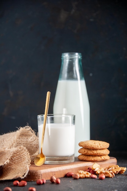 Foto gratuita vista de cerca de una leche fresca en un vaso y una botella de galletas en una tabla de madera toalla de color nude nueces cacahuetes sobre fondo oscuro