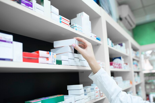 Vista de cerca de la mano del farmacéutico tomando la caja de la medicina del estante en la farmacia