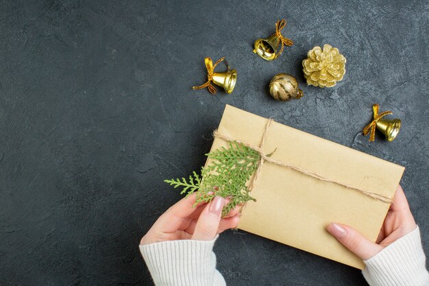 Vista de cerca de la mano que sostiene la caja de regalo y accesorios de decoración sobre fondo oscuro