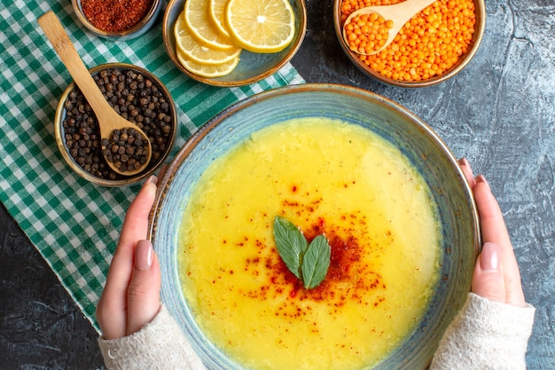 Vista de cerca de la mano que sostiene un plato azul con una sabrosa sopa servida con menta y pimienta sobre una toalla verde despojado