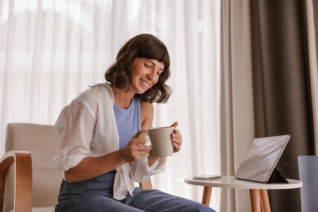 Vista de cerca de una mujer caucásica mirando y sonriendo a una taza de café