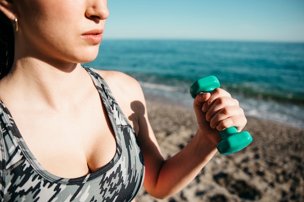 Vista de cerca de mujer entrenando con pesas en la playa