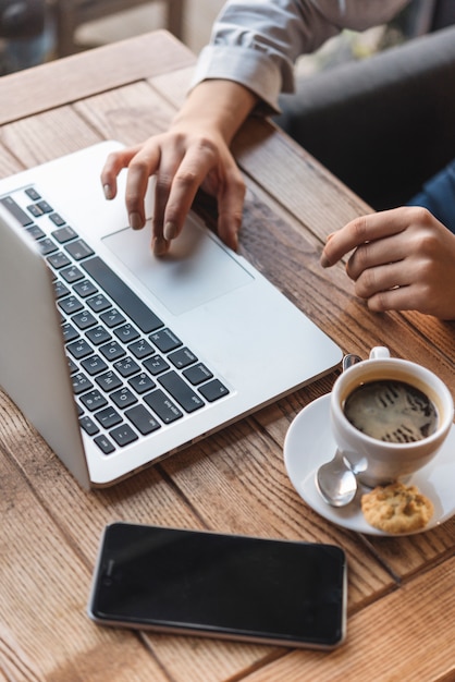 Vista de cerca de mujer escribiendo en portátil en cafetería