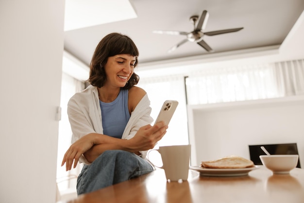 Vista de cerca de una mujer sentada en la cocina sonriendo al teléfono