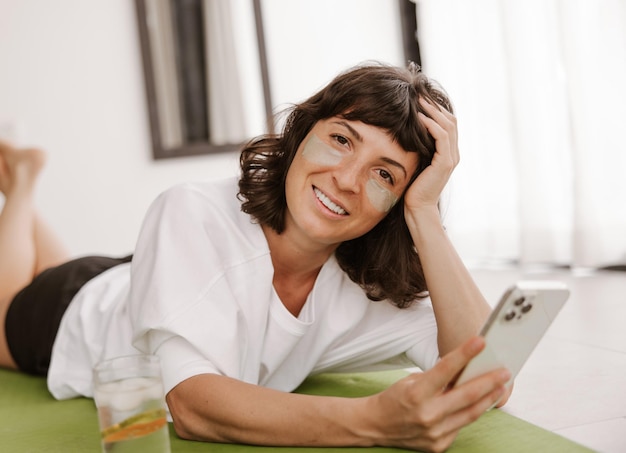 Vista de cerca de una mujer sonriente con parches de gel verde con teléfono