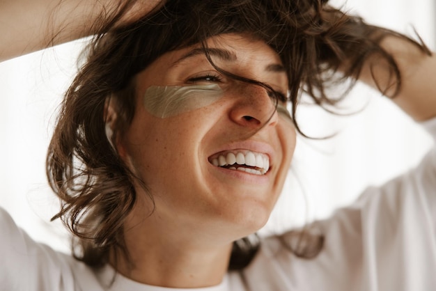 Vista de cerca de una mujer sonriente con parches verdes en casa con los ojos cerrados