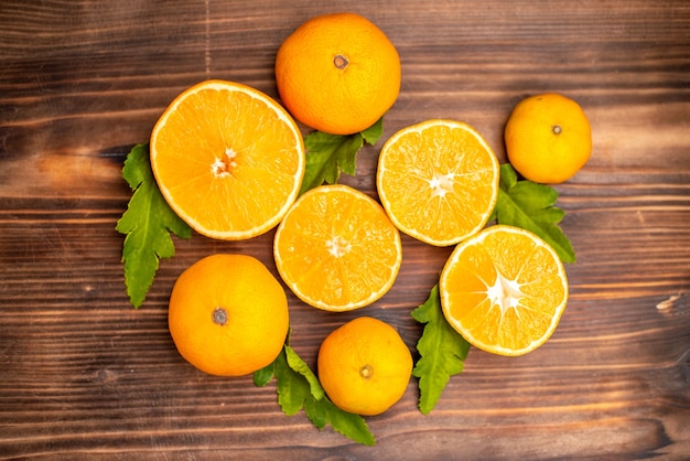 Vista de cerca de naranjas frescas enteras y cortadas con hojas sobre un fondo marrón