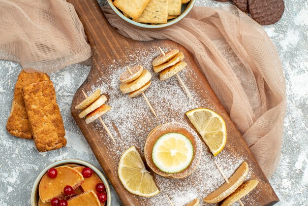 Vista de cerca de panqueques simples con limones en tabla de cortar y galletas toalla naranja sobre azul