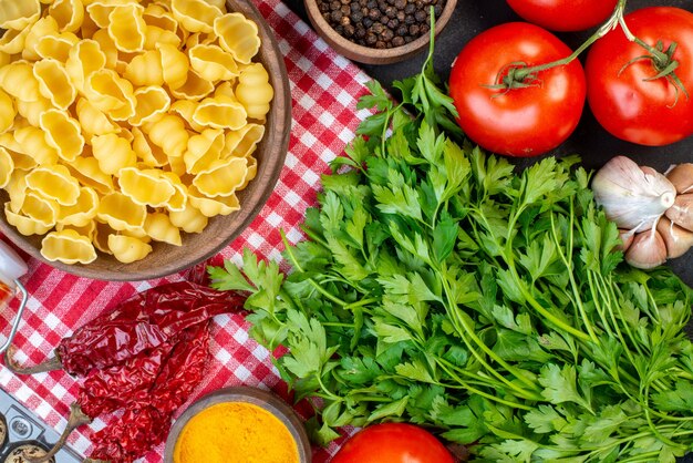 Vista de cerca de pastas crudas en tomates frescos despojados rojos jengibre amarillo pimiento seco un paquete verde sobre mesa negra