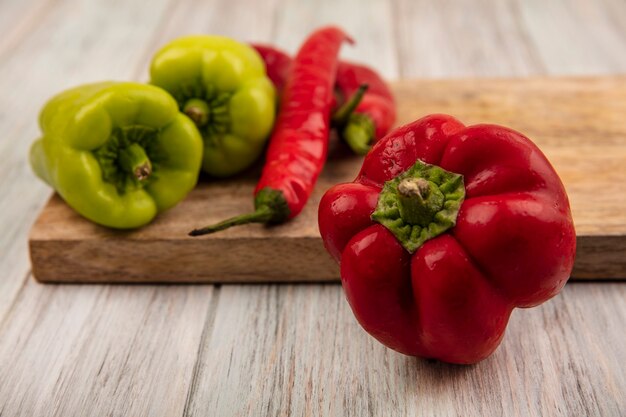 Vista de cerca de un pimiento rojo fresco con coloridos pimientos y ají en una placa de cocina de madera sobre un fondo de madera gris