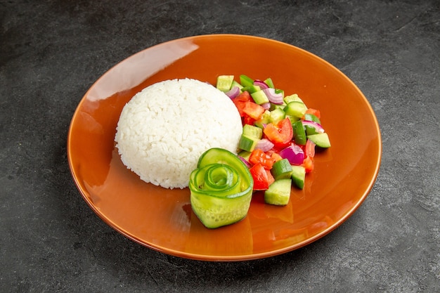 Vista de cerca del plato de arroz casero y ensalada con tomate y pepino en la oscuridad