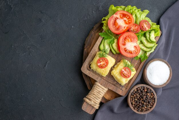 Vista de cerca de queso de verduras frescas picadas en la tabla de cortar y especias en una toalla de color oscuro sobre la superficie negra