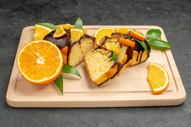 Vista de cerca de rodajas de naranja fresca y rodajas de pastel picadas en la mesa oscura