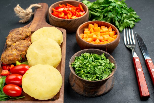 Vista de cerca de sabrosas chuletas con verduras con tenedor y cuchillo en la oscuridad