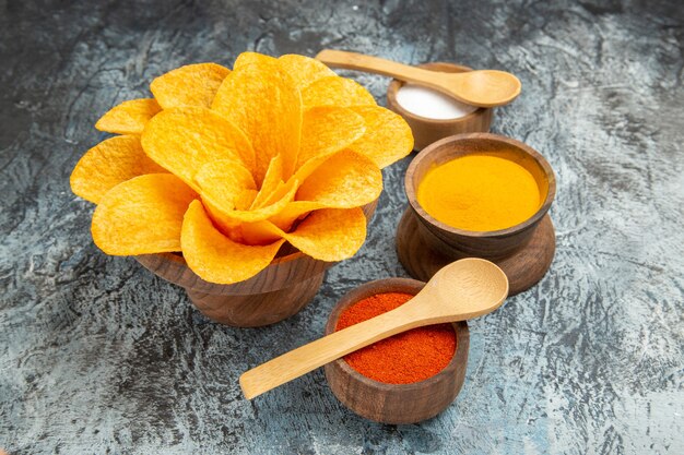 Vista de cerca de sabrosas papas fritas decoradas como diferentes especias en forma de flor con cucharas sobre ellos en la mesa gris