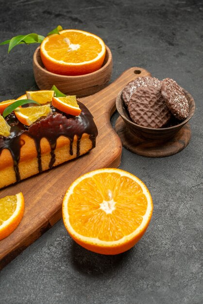 Vista de cerca de sabrosos pasteles cortan naranjas con galletas en la tabla de cortar en la mesa oscura