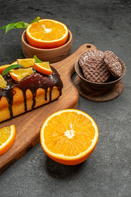 Vista de cerca de sabrosos pasteles cortan naranjas con galletas en la tabla de cortar en la mesa oscura