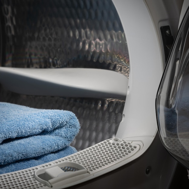 Vista de cerca de una secadora de ropa con toallas azules en el interior y una lavadora de puertas abiertas en una habitación oscura con un tambor bien iluminado Foto Premium 