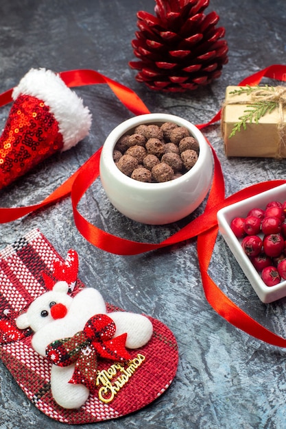 Vista de cerca del sombrero de santa claus y el calcetín de año nuevo de chocolate cornel regalo de cono de conífera roja sobre superficie oscura