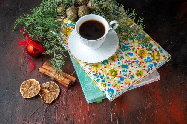 Vista de cerca de una taza de té negro en dos libros, limas canela y accesorios de decoración de ramas de abeto sobre fondo oscuro