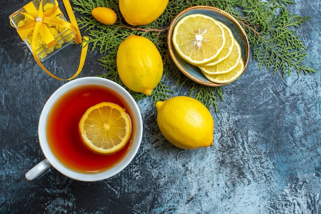 Vista de cerca de una taza de té negro con limón y colección de medio cítricos enteros en cajas de regalo de ramas de abeto sobre fondo oscuro