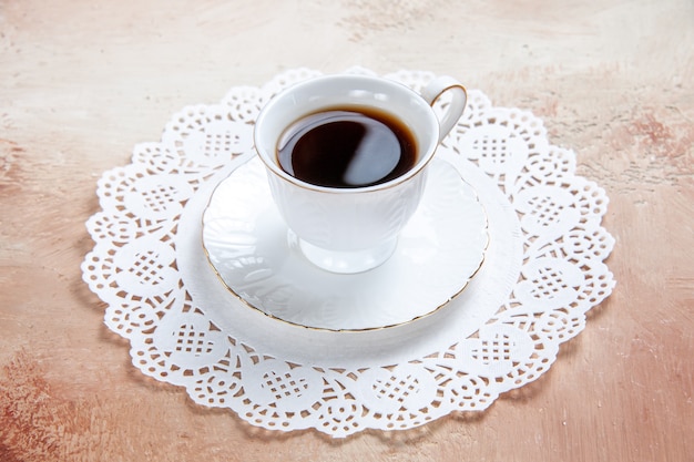 Vista de cerca de una taza de té negro sobre una servilleta decorada en blanco en colores