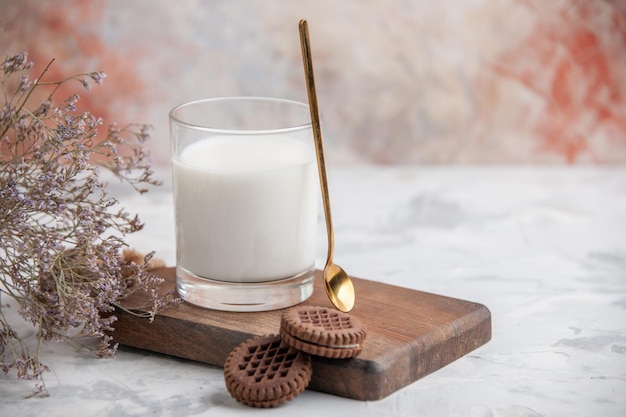 Vista de cerca del vaso de vidrio lleno de leche y galletas en la flor de la tabla de madera sobre fondo de hielo