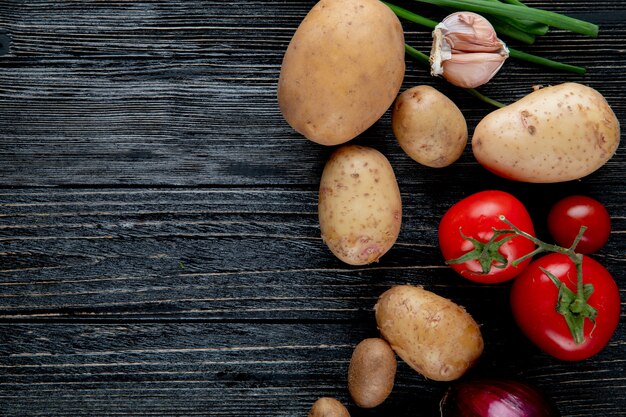 Vista de cerca de verduras como patata ajo tomate en el lado derecho y fondo de madera con espacio de copia