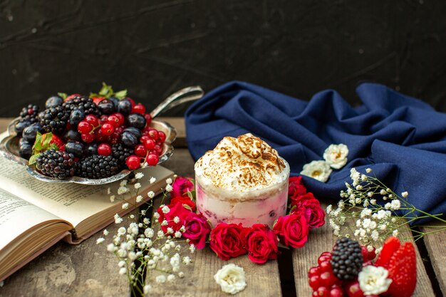 Una vista cercana de cerca delicioso postre alrededor de rosas rojas y bayas frescas en el escritorio rústico de madera marrón