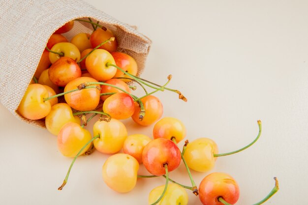 Vista cercana de cerezas amarillas derramándose de saco sobre superficie blanca