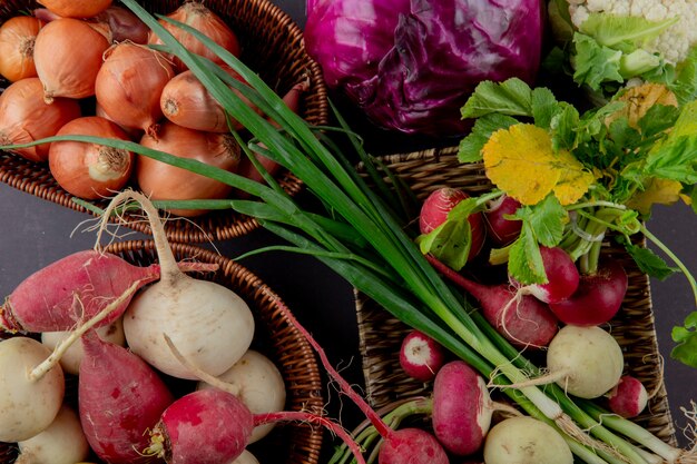 Vista cercana de cestas y plato de verduras como cebolla, rábano, cebollín y repollo sobre fondo marrón