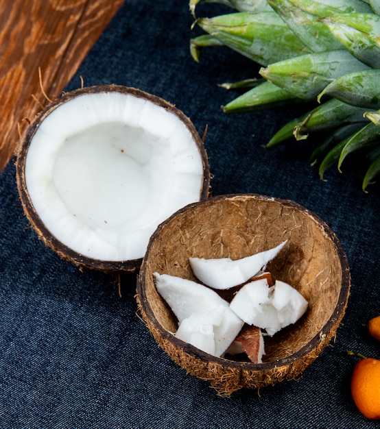 Vista cercana de cítricos como coco medio cortado con rodajas de coco en cáscara kumquats piña sobre fondo de tela de jeans