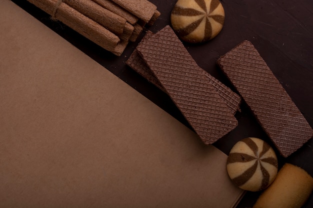 Foto gratuita vista cercana del cuaderno de bocetos con diferentes galletas alrededor de maffins de pan de jengibre y palitos crujientes en la oscuridad