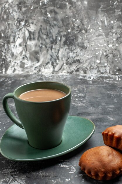 Vista cercana de delicioso café y dos pasteles en una taza verde sobre gris