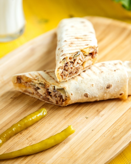 Vista cercana de doner de pollo envuelto en lavash con pimiento verde en escabeche en bandeja de madera