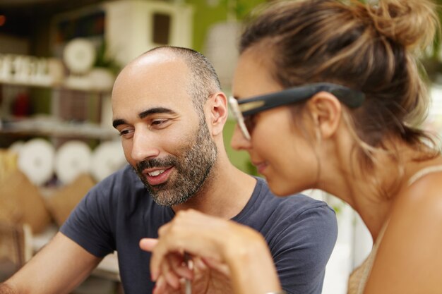 Vista cercana de dos amigos que pasan tiempo libre juntos, miran algo en línea en algún dispositivo electrónico, navegan por Internet, disfrutan de wi-fi gratis, se sientan en un restaurante en la acera durante el almuerzo