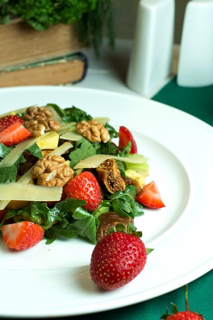 Vista cercana de ensalada fresca con queso parmesano, aguacate, nueces, tomates cherry y fresas en un tazón blanco