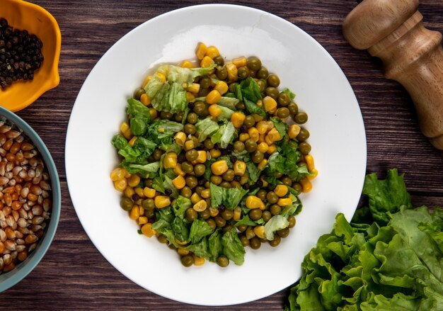 Vista cercana de ensalada de maíz con semillas de maíz semillas de pimienta negra y lechuga en la mesa de madera