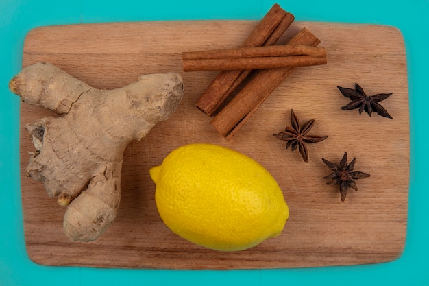 Foto gratuita vista cercana de especias como jengibre y canela con limón en la tabla de cortar sobre fondo azul.