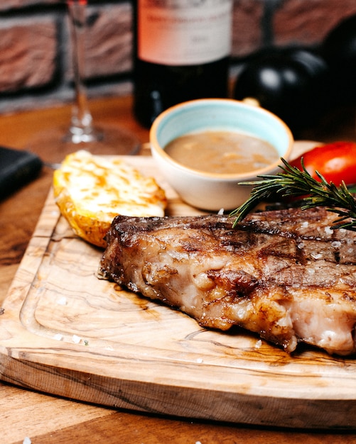 Vista cercana de filete de ternera a la parrilla servido con verduras y salsa sobre tabla de madera