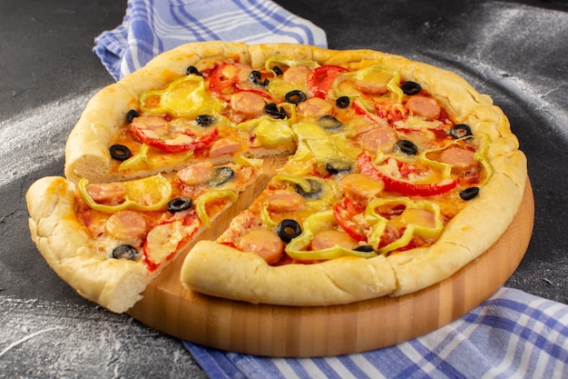 Vista cercana frontal sabrosa pizza cursi con tomates rojos, aceitunas negras y salchichas en el oscuro escritorio