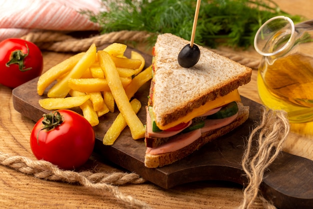 Vista cercana frontal sabroso sandwich con aceitunas, jamón y tomates junto con papas fritas