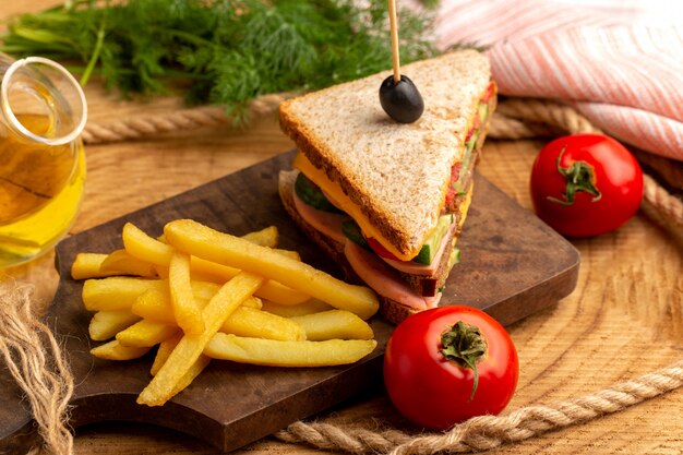 Vista cercana frontal sabroso sandwich con aceitunas, jamón y tomates junto con papas fritas