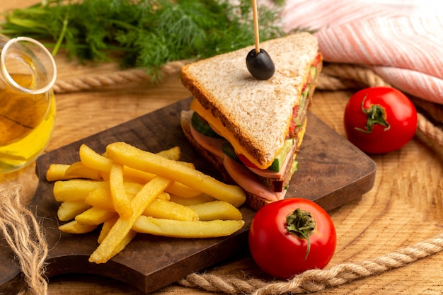 Vista cercana frontal sabroso sandwich con aceitunas, jamón y tomates junto con papas fritas