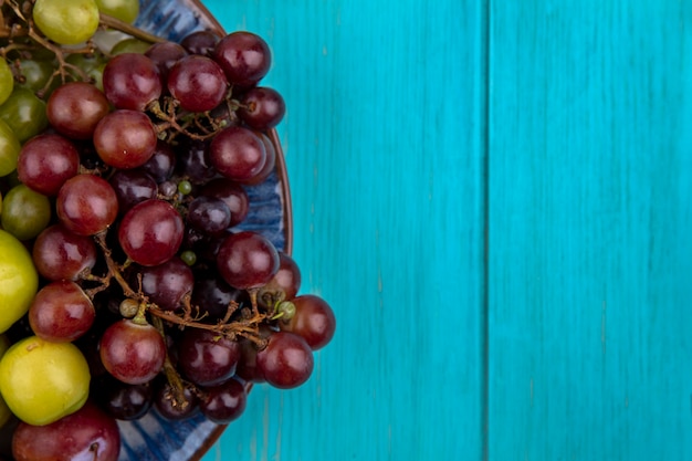 Foto gratuita vista cercana de frutas como ciruelas y uvas en placa sobre fondo azul con espacio de copia