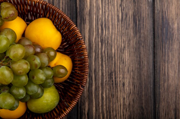 Vista cercana de frutas como pluot verde uva y nectacots en canasta sobre fondo de madera con espacio de copia